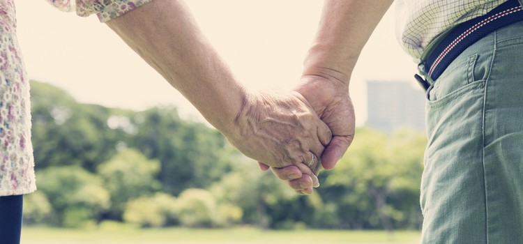 A close up of an older couple holding hands in a park
