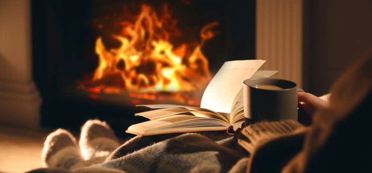 Someone sitting in front of a fire with a book and cup of tea.