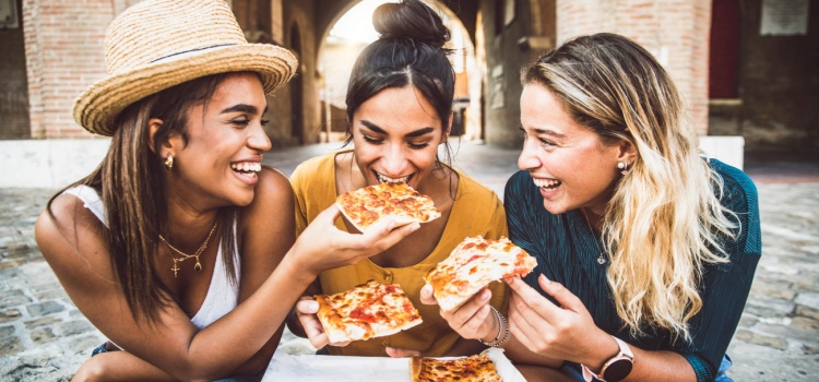 Three women eating pizza in an exotic location